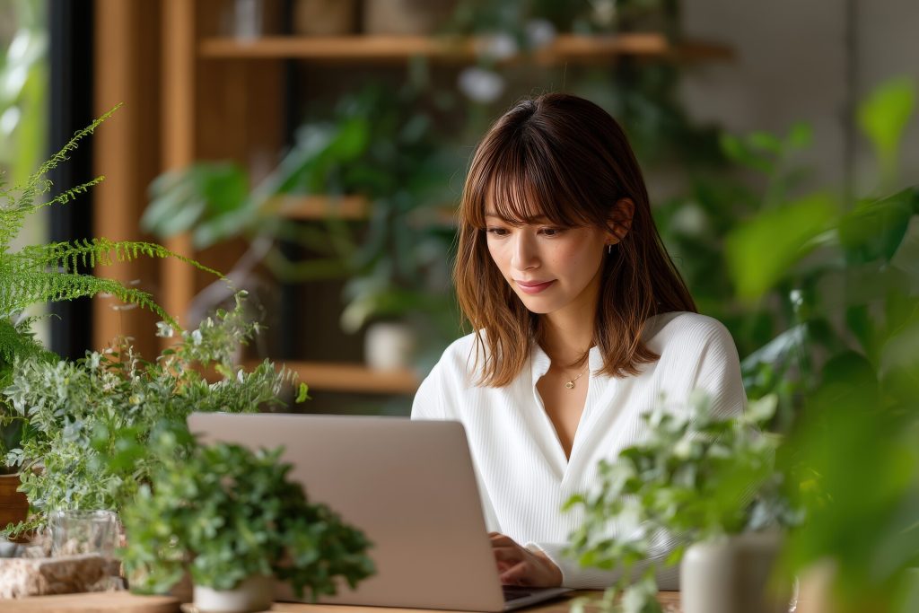 Young woman works on laptop surrounded by green plants indoor